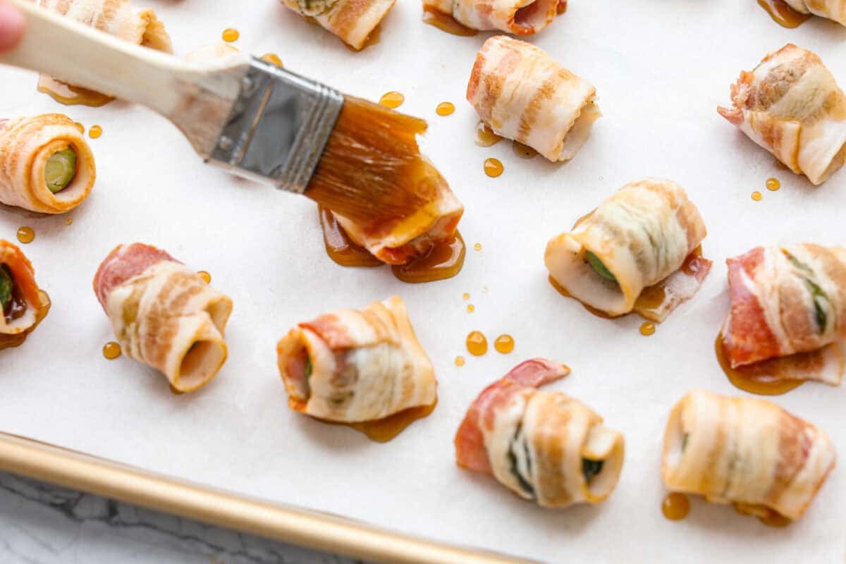 Someone brushing the maple drizzle onto the bacon wrapped Brussels sprouts. 