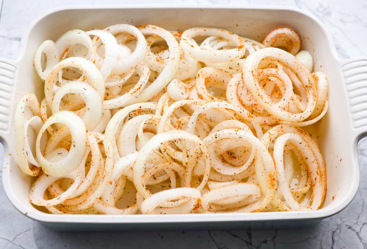 Seasoned onions spread out in a 9x13 baking dish. 
