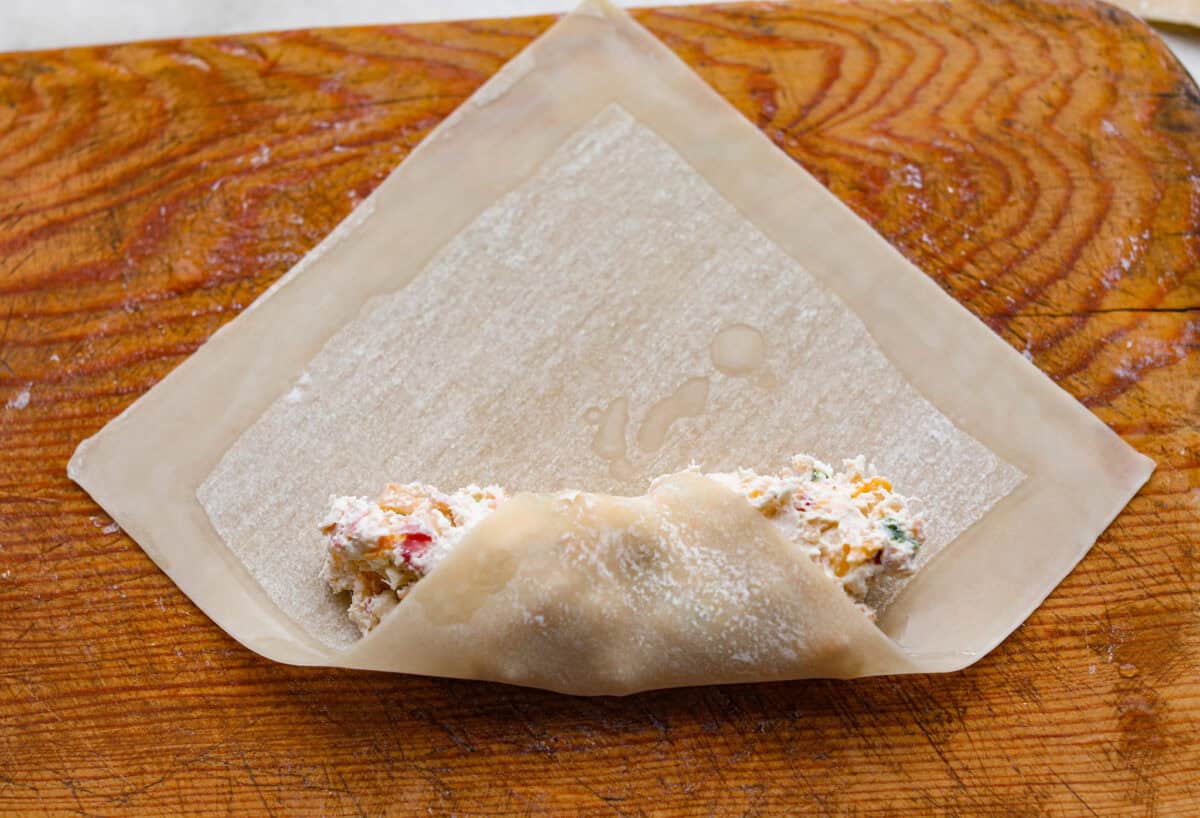 Egg roll wrapper with water lining the edges, and one corner wrapping around the filling. 