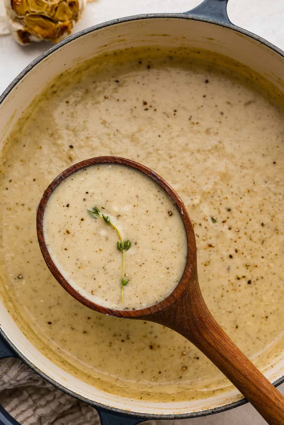 Creamy roasted garlic soup is comfort food with a side of obsession. Combining roasted garlic, tender potatoes, and nutty Parmesan into a cozy soup is absolute perfection. Just make sure you serve it to anyone within hugging distance. Pot of roasted garlic soup with wooden ladle.