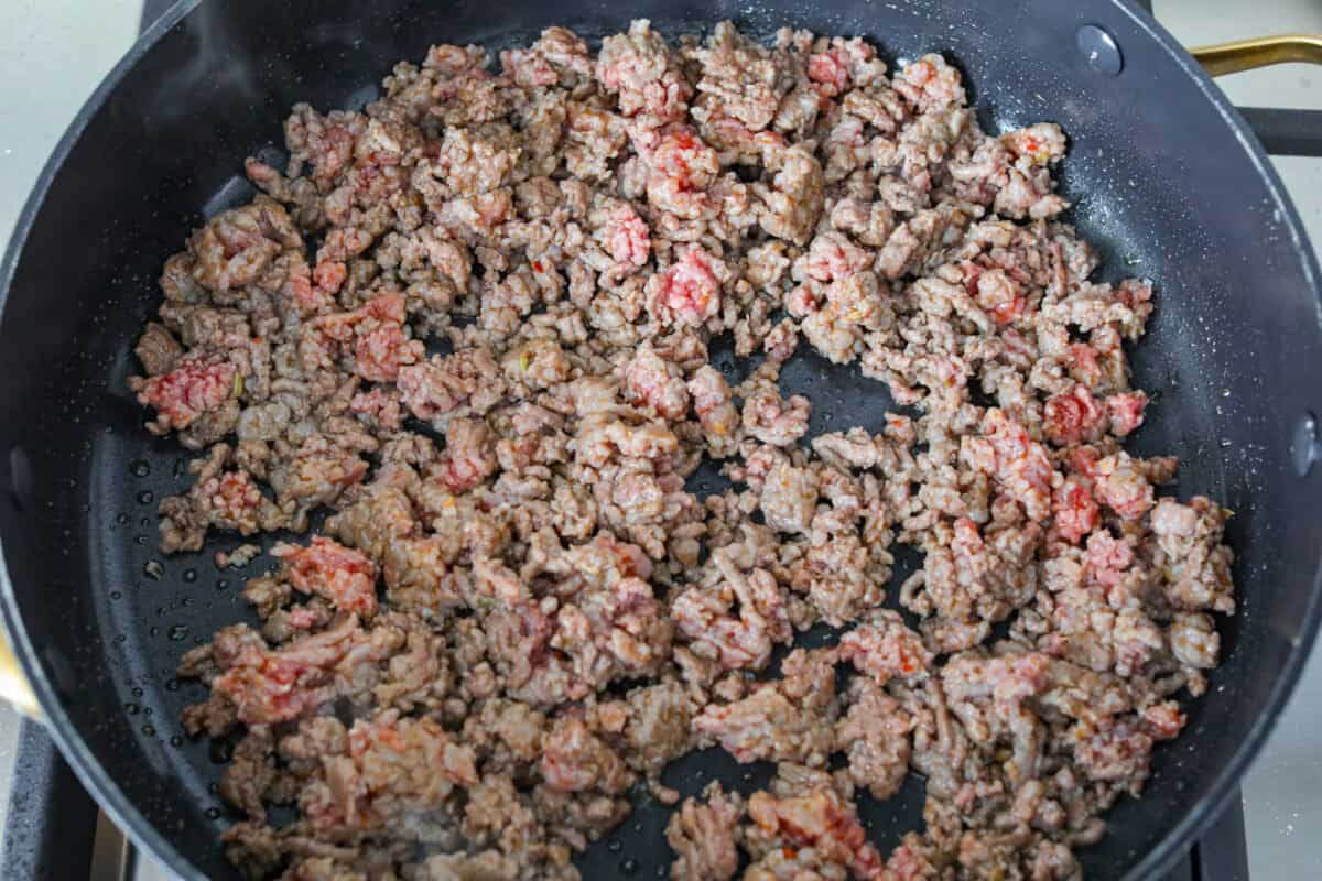 Ground beef and Italian sausage cooking in a skillet. 