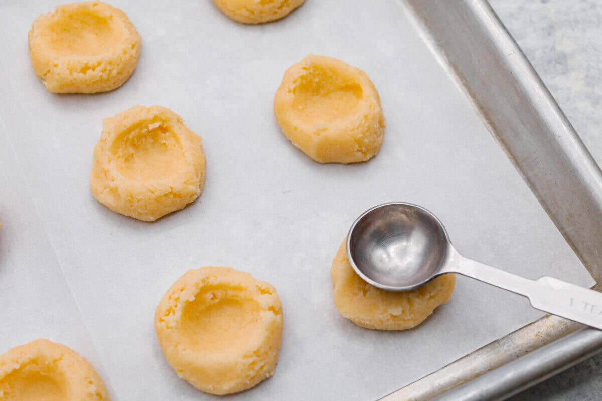 Someone pressing the bottom of a rounded teaspoon into the top of the cookie dough ball before its baked. 