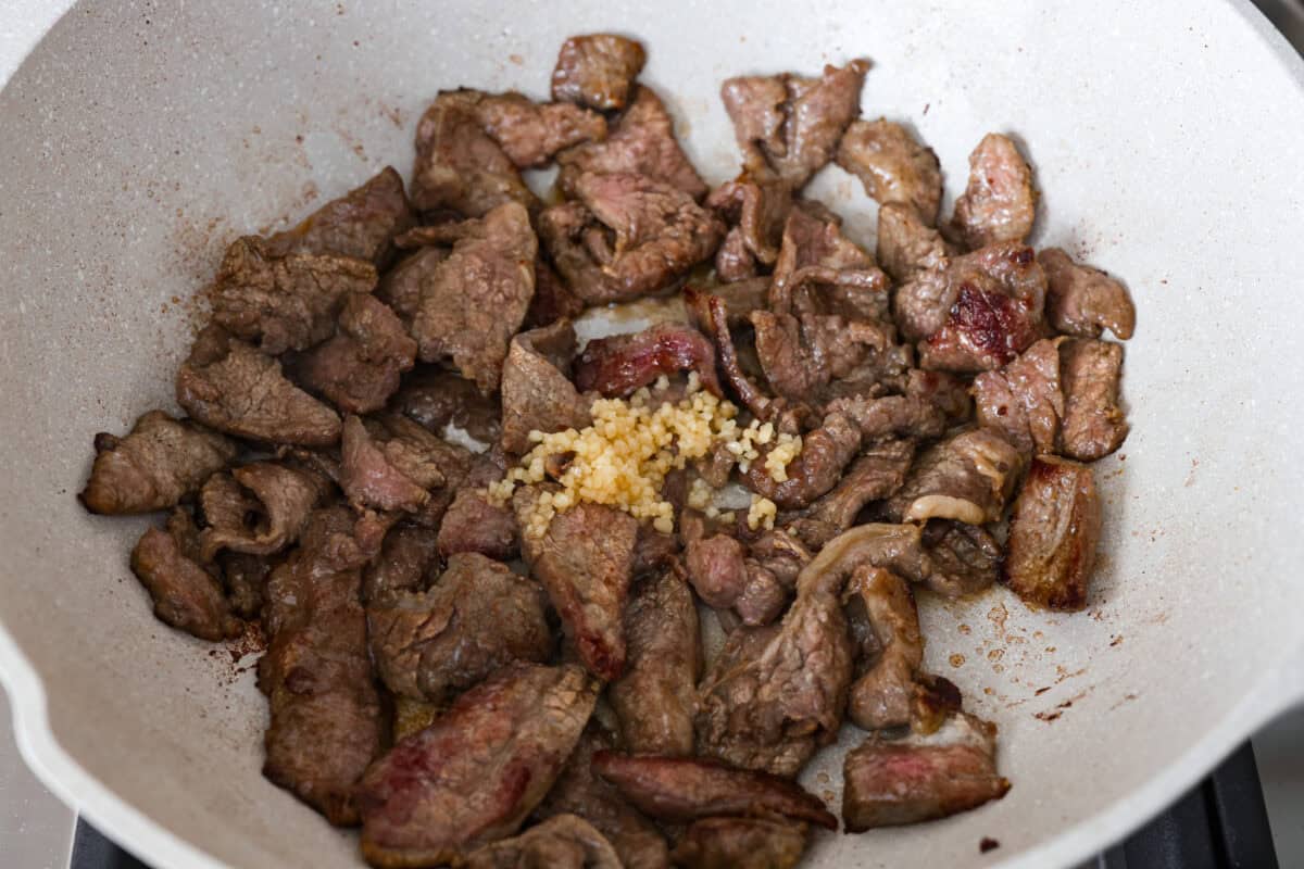 Beef cooking in a skillet with garlic. 