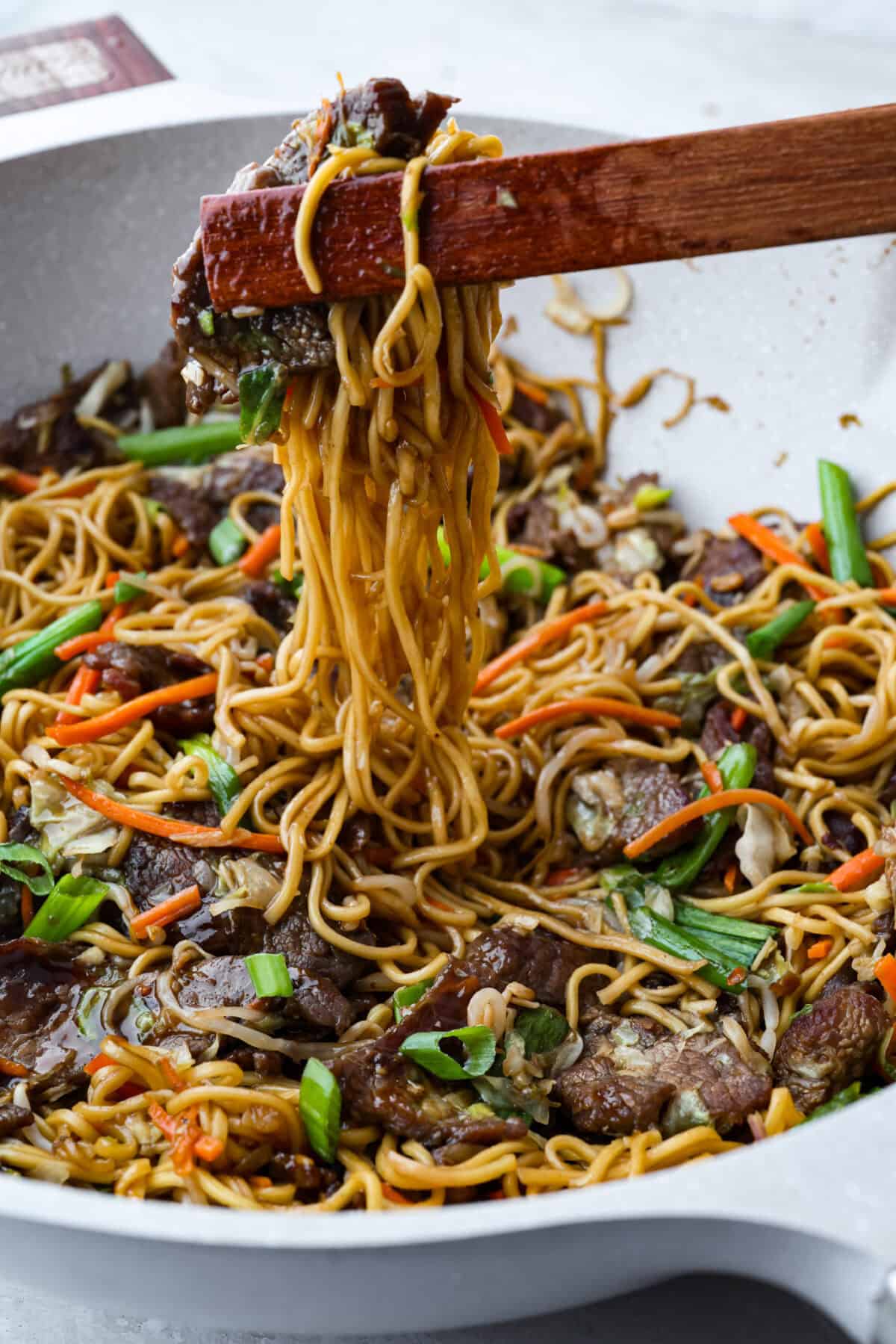 Side shot of someone pulling up a scoop of beef chow mein from the skillet. 