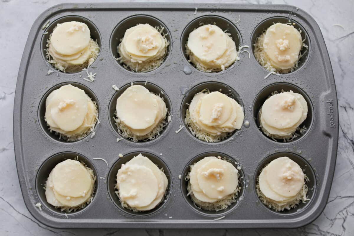 Potato slices stakced in a muffin tin with the butter sauce and cheese in between the layers. 