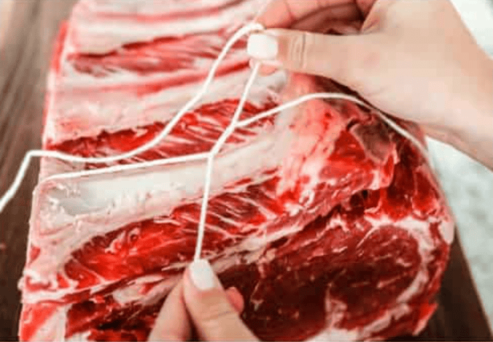 Someone tying the prime rib with butchers twine.