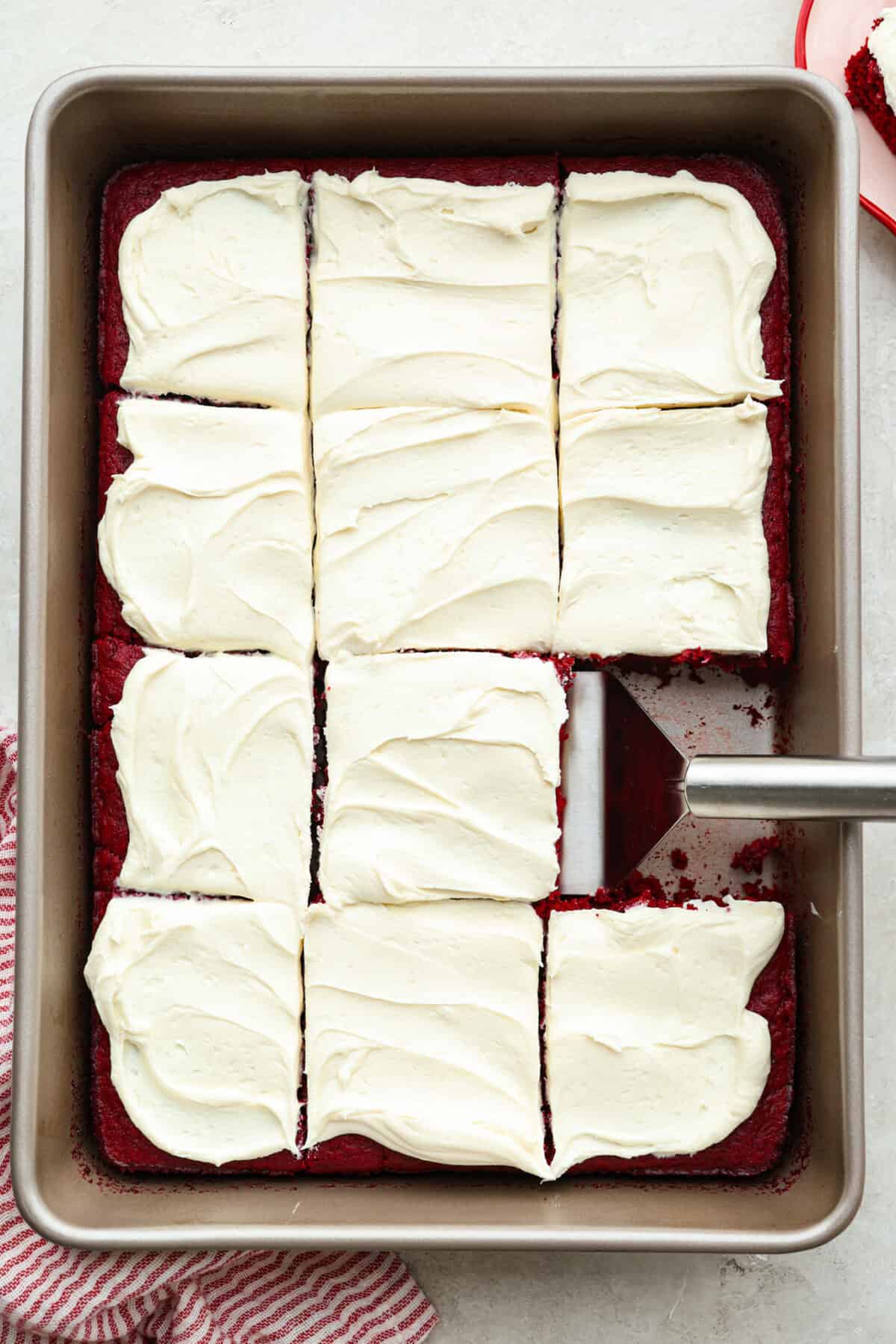 This 2-ingredient red velvet cake is almost too easy to believe! With just a cake mix and a can of soda, you can make a soft, fluffy cake in minutes. It’s the perfect shortcut dessert for Valentine’s Day or any sweet craving! Overhead shot of the 2 ingredient red velvet cake frosted, sliced and someone using a spatula to lift a piece out.