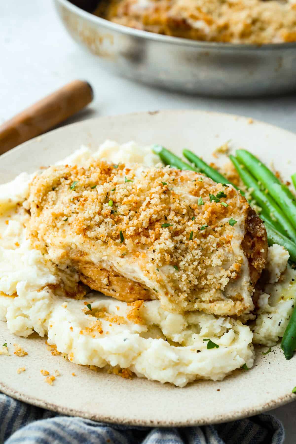 Plated copycat longhorn parmesan crusted chicken on mashed potatoes and next to green beans.