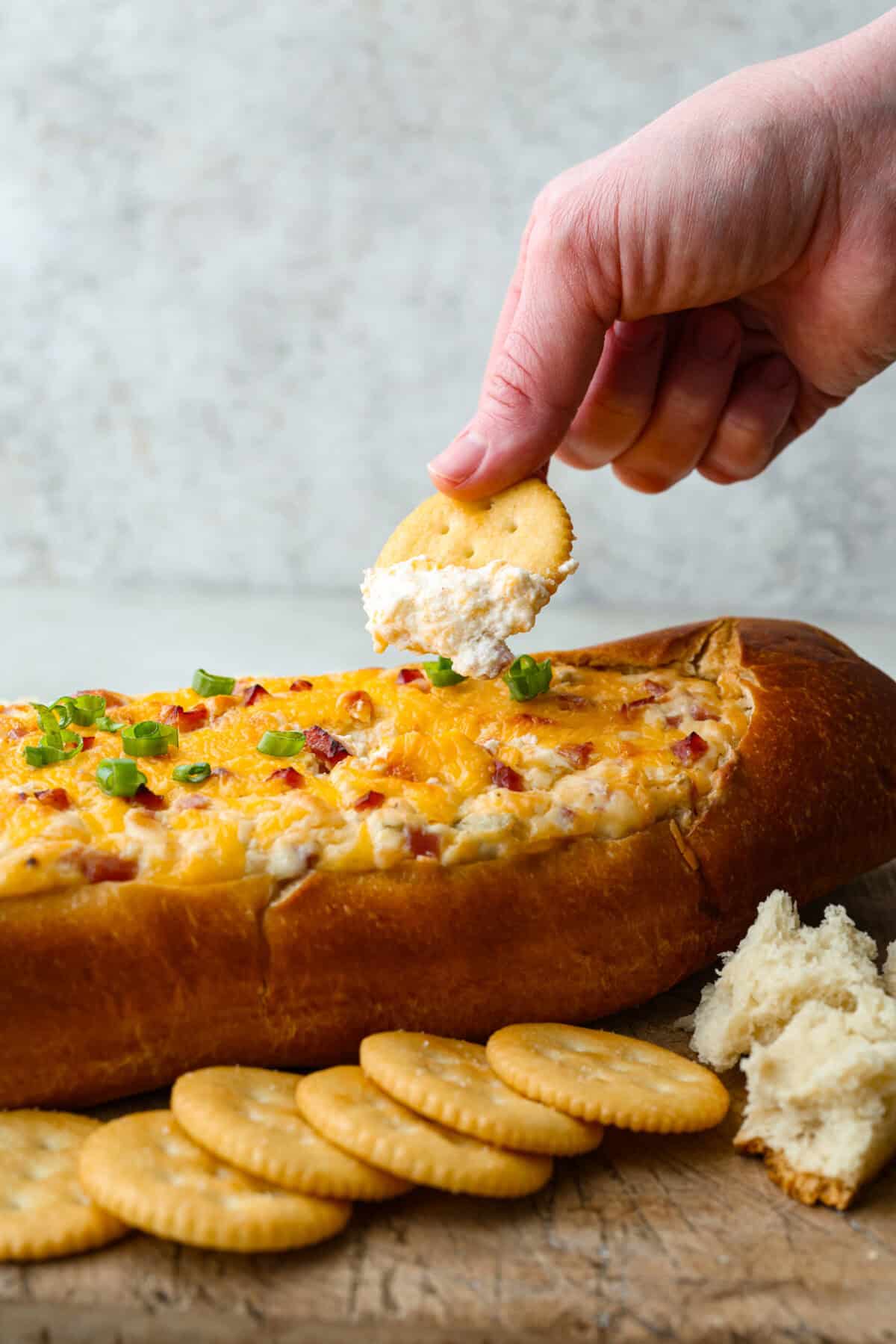 This Mississippi sin dip is pure comfort-food goodness. Creamy, cheesy, a little smoky, and baked into a loaf of French bread, it’s the kind of snack everyone gathers around and keeps going back for! Someone scooping a bite of Mississippi sin dip from the loaf.