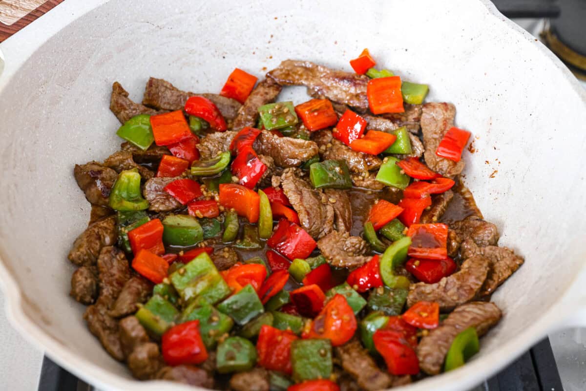 Steak, peppers, and sauce all cooking in a wok.