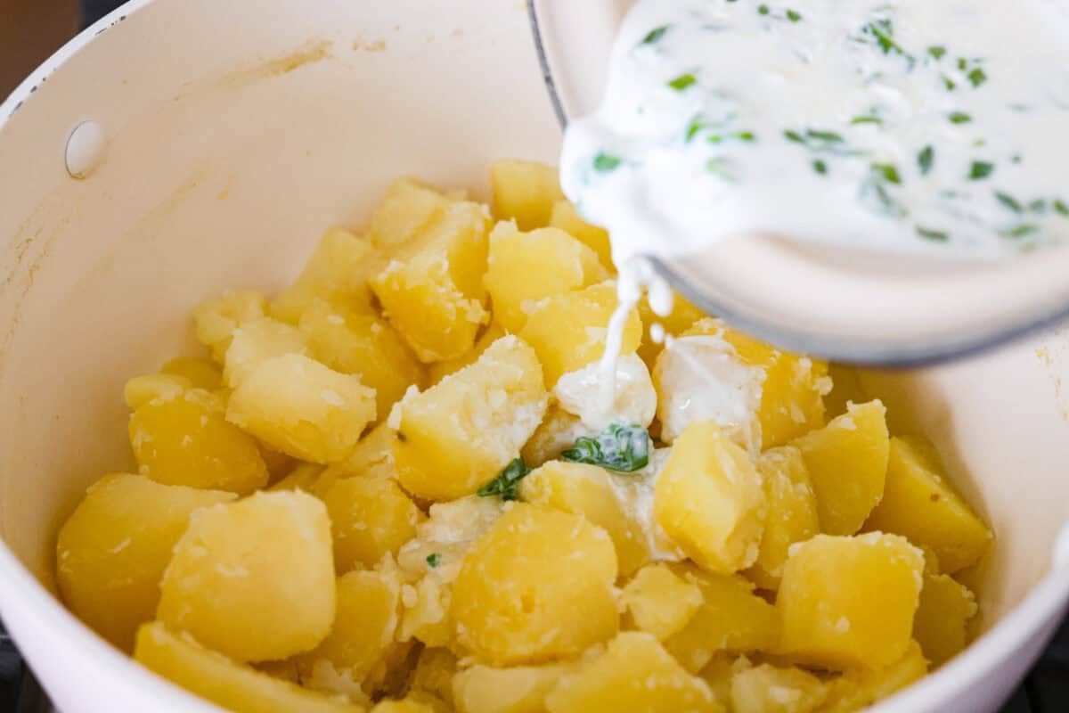 Irish champ potatoes are mashed potatoes done right. Fluffy spuds meet warm onion kissed milk and a generous melt of Irish butter for a side that’s simple, rustic, and seriously so good! Someone pouring the onion infused milk into the boiled potatoes.