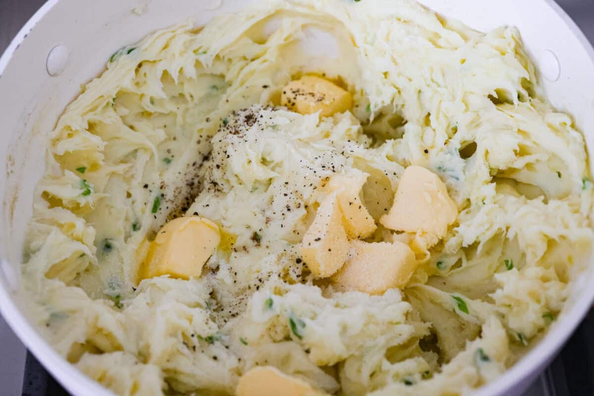 Irish champ potatoes are mashed potatoes done right. Fluffy spuds meet warm onion kissed milk and a generous melt of Irish butter for a side that’s simple, rustic, and seriously so good! Butter, salt, and pepper added to the mashed potatoes.