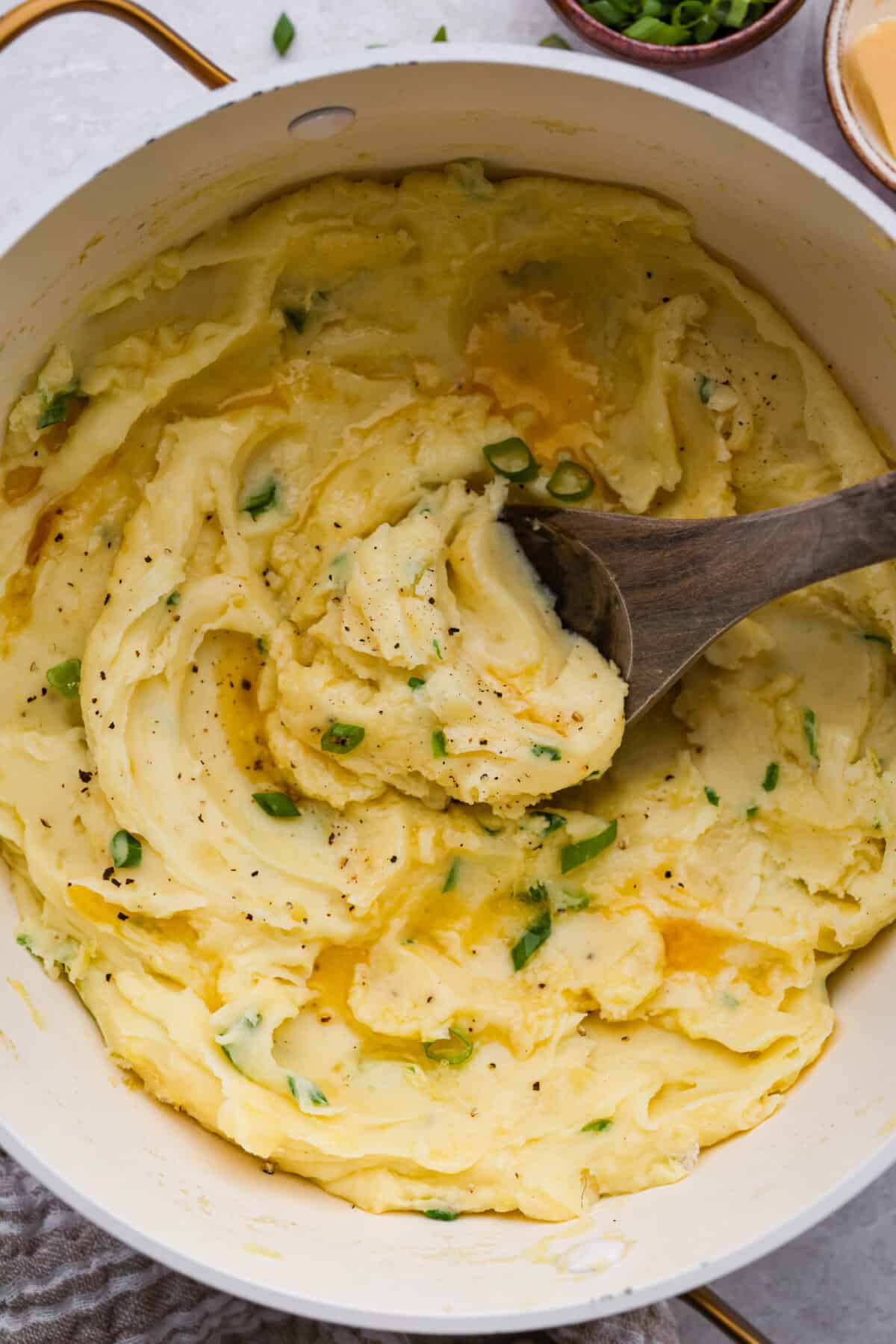 Irish champ potatoes are mashed potatoes done right. Fluffy spuds meet warm onion kissed milk and a generous melt of Irish butter for a side that’s simple, rustic, and seriously so good! Irish champ potatoes in a saucepan with a wooden spoon.