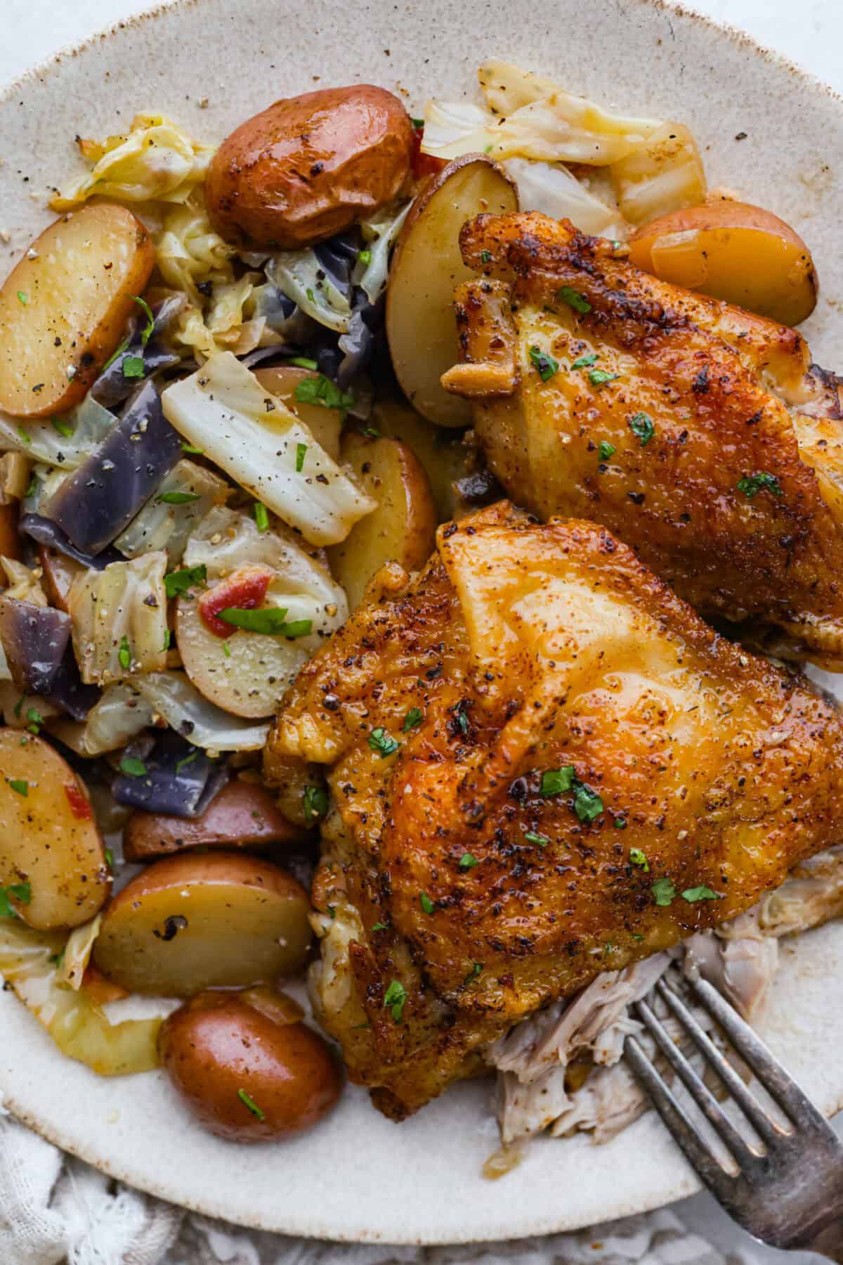 This Irish chicken is my cozy mashup of pub vibes and weeknight reality. Seared chicken thighs baked over bacon, cabbage, and potatoes, then I add a splash of Irish whiskey and a touch of cream to make the whole pan taste extra special. Plated Irish chicken next to the cabbage ad potatoes.