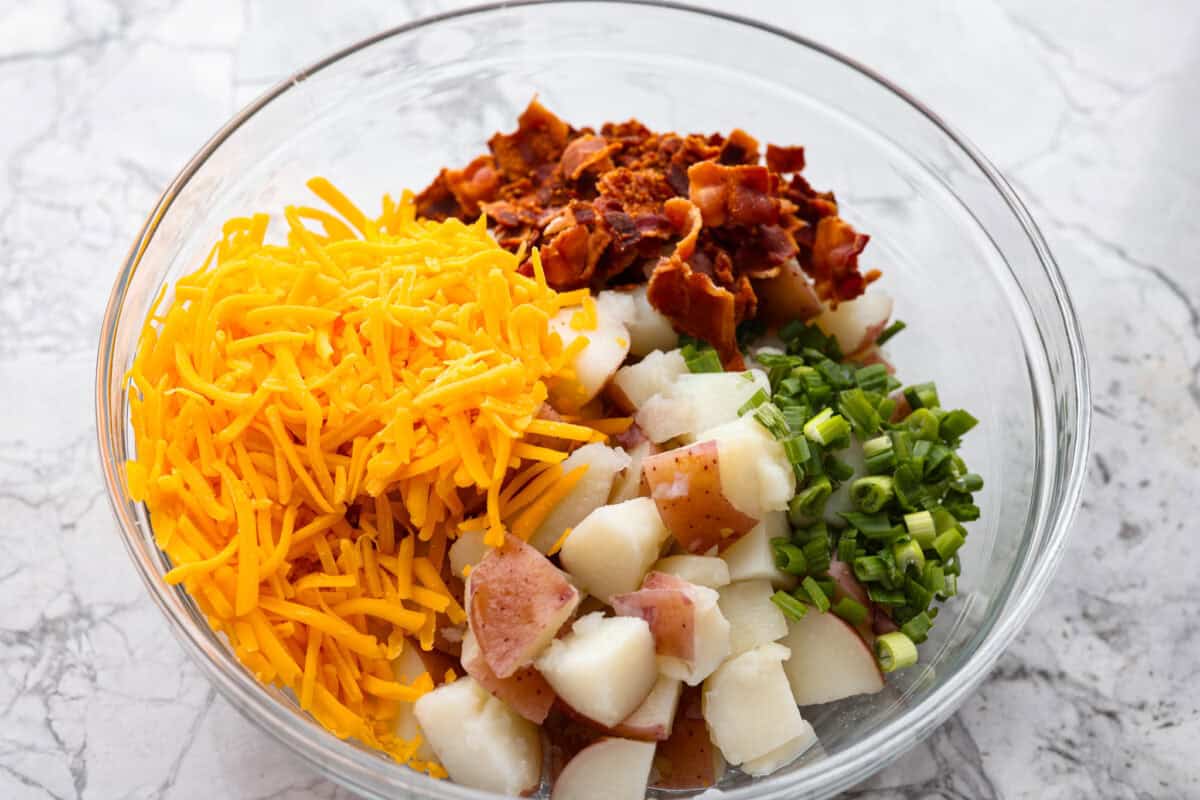 Cooked potatoes, cheese, green onions all added to a bowl. 