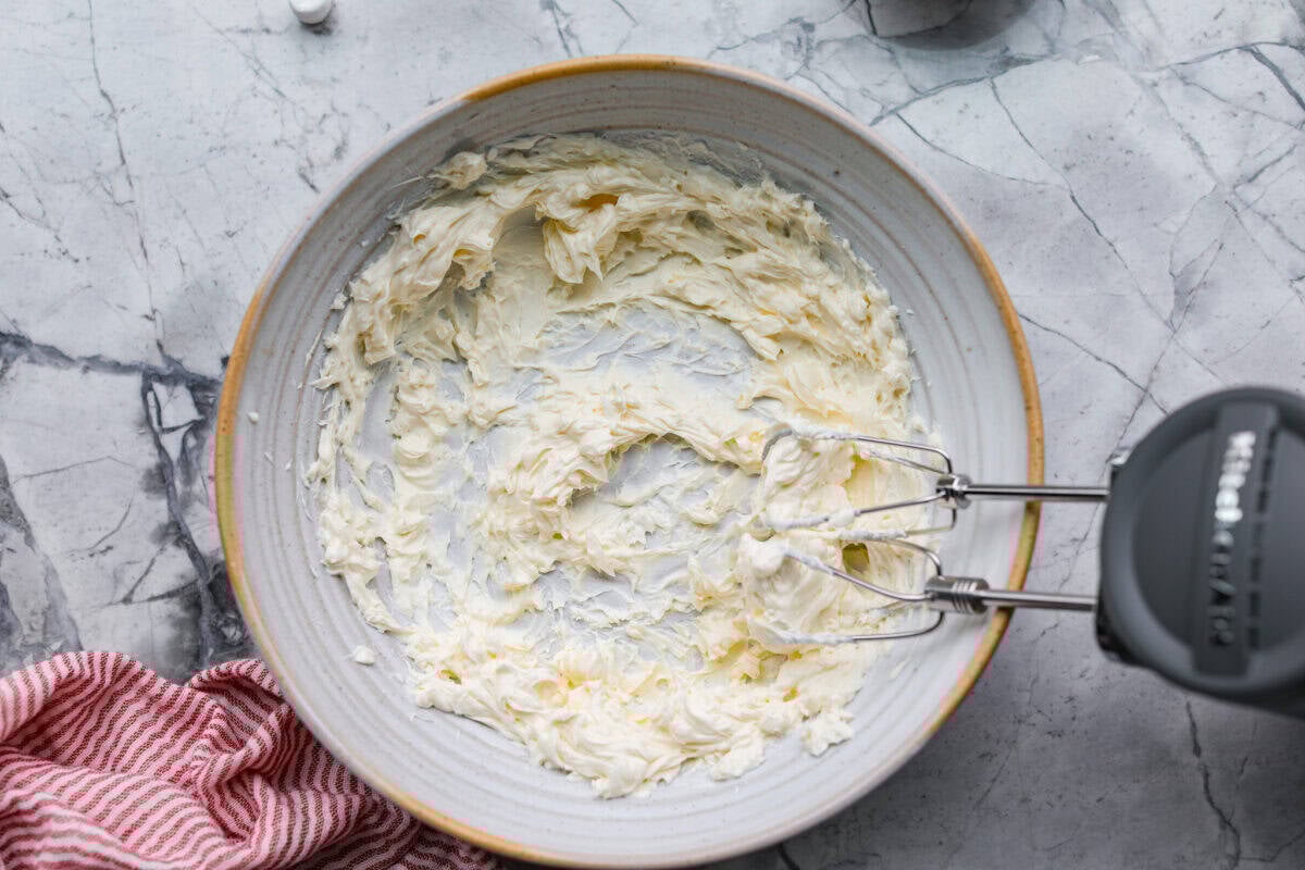 Cream cheese mixed in a bowl with a hand mixer. 