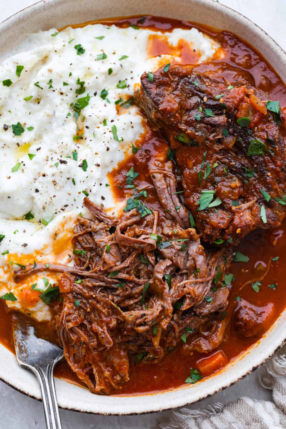Meet Stracotto, the Italian pot roast you didn't know you were missing! A seared roast is slowly braised in a rich, hearty tomato sauce until it is melt-in-your-mouth tender. The sauce alone is worth making this recipe for! Plated Italian Pot Roast next to some polenta.
