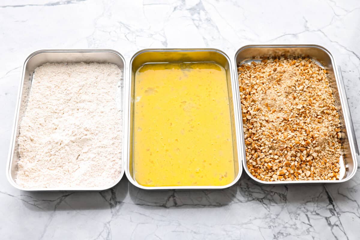 This pretzel crusted chicken takes crispy chicken to the next level. The crunchy pretzel coating adds incredible flavor and texture, making every bite extra delicious. Coating station set up with flour, egg, and pretzel mixtures in separate containers.