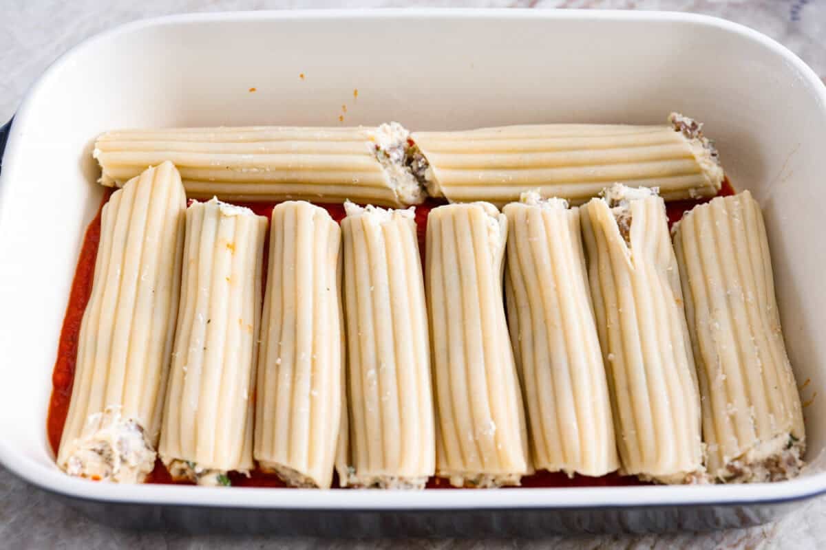 Stuffed manicotti shells in a baking dish on top of the marinara sauce. 
