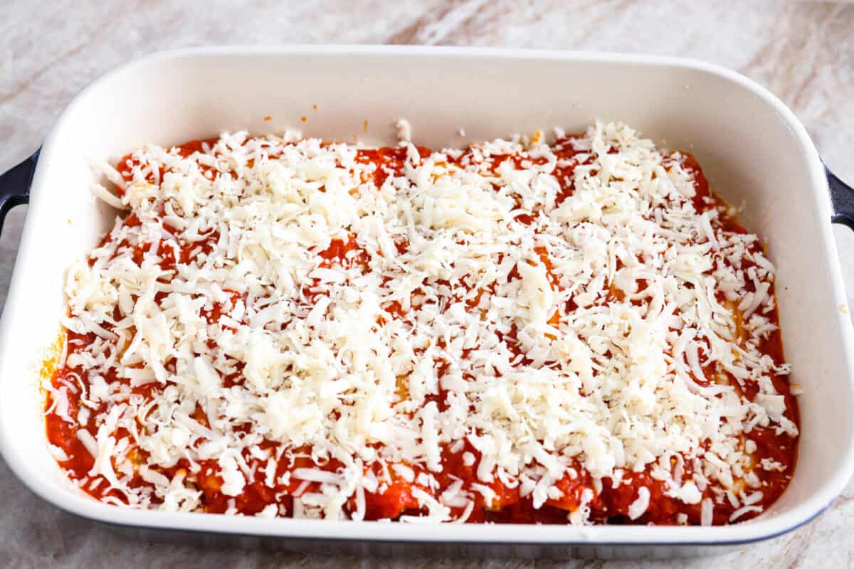 Marinara sauce and shredded cheese on top of the stuffed manicotti. 