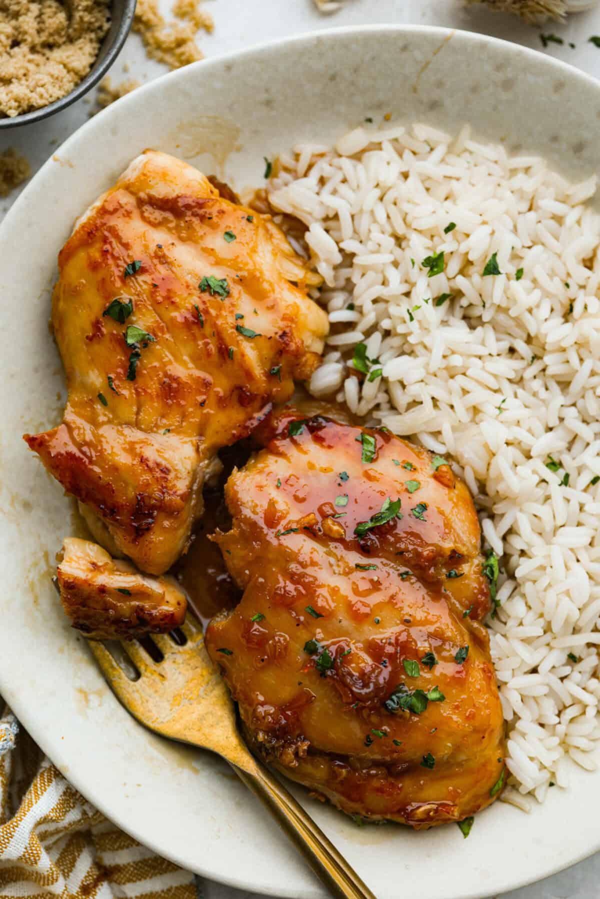 Plated brown sugar chicken thighs next to a bed of rice. 