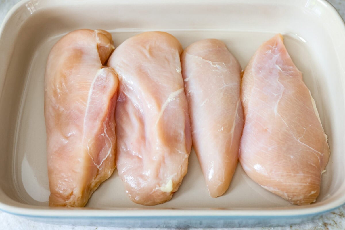 Chicken breasts in a row in a baking dish.