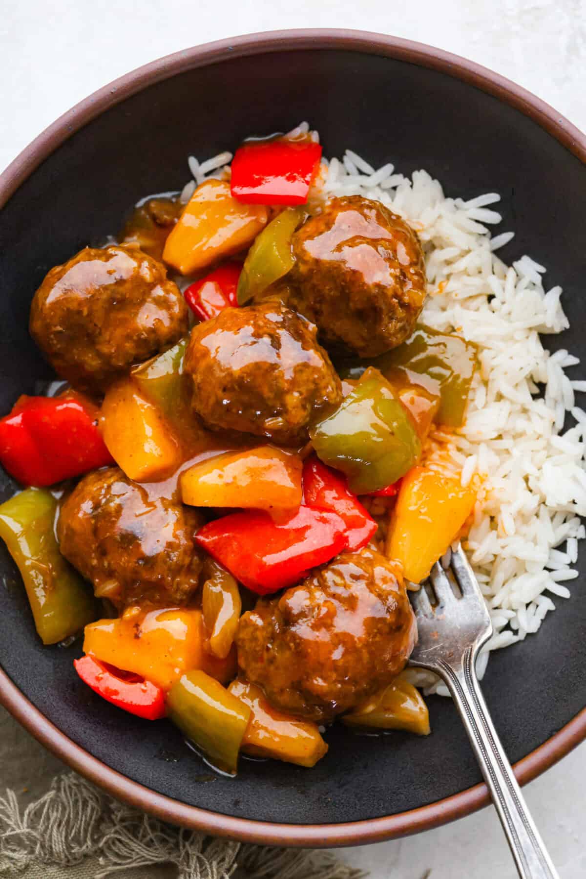 Bowl with a serving of sweet and sour meatballs on a bed of rice.