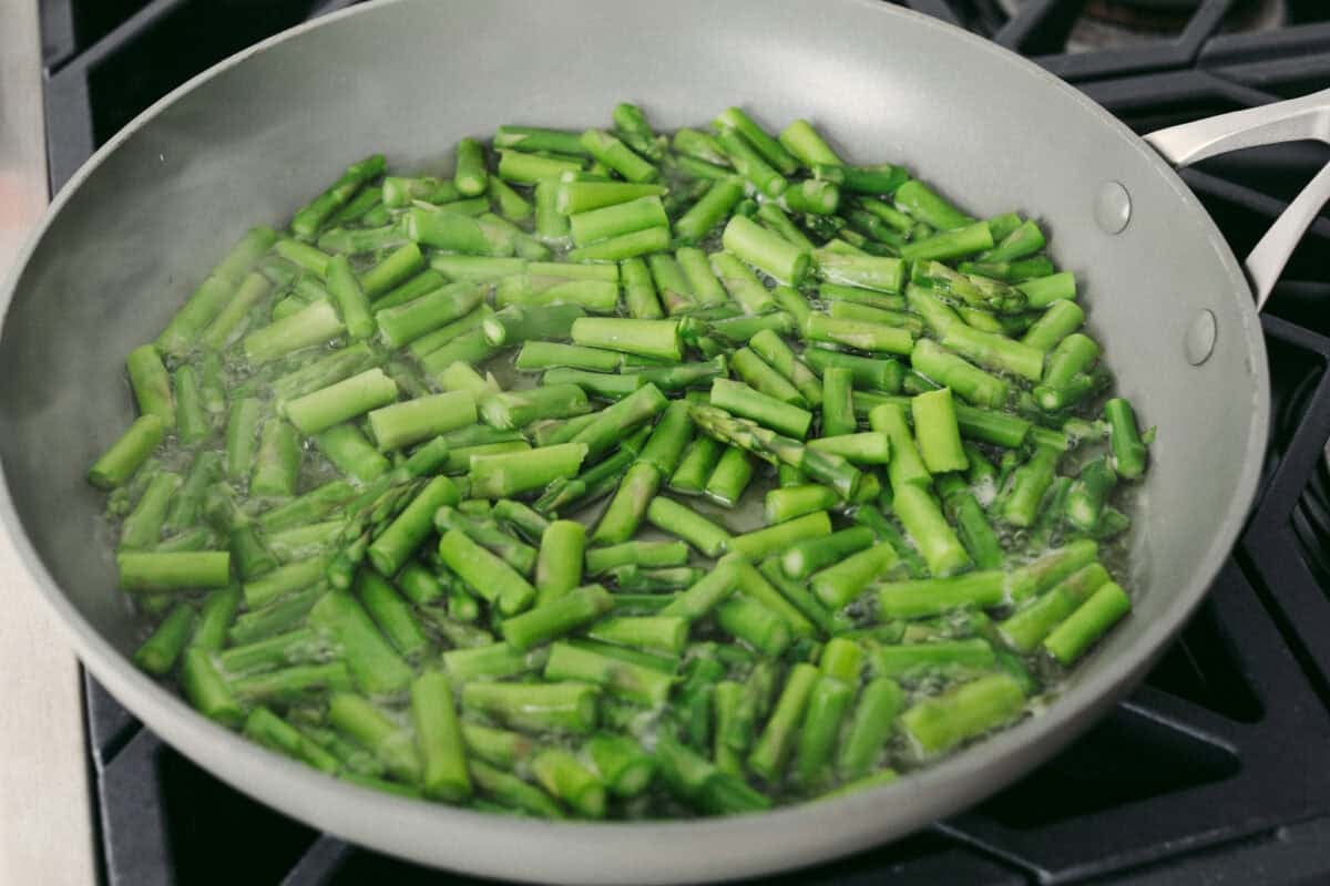 Asparagus cooking in a skillet on the stove. 