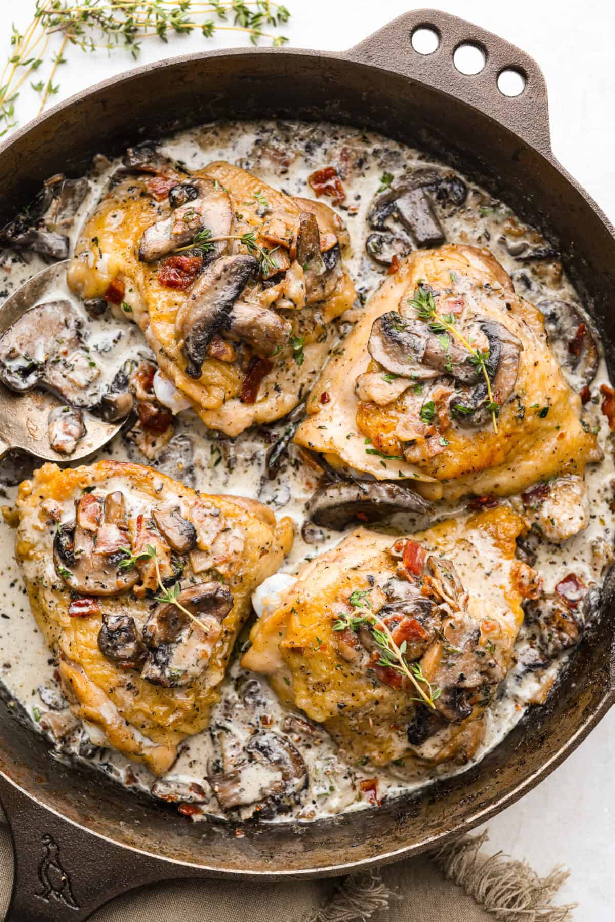 If cozy dinners are your thing, this creamy bacon mushroom thyme chicken needs to happen soon. Between the crispy chicken skin, smoky bacon, and creamy mushroom sauce, every bite tastes rich and savory. Perfect for spooning over mashed potatoes! Skillet with bacon mushroom thyme chicken thighs cooked and covered in a creamy mushroom sauce.