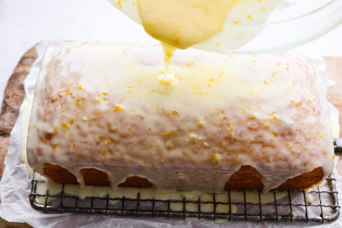 Someone pouring the orange glaze over the baked orange loaf. 