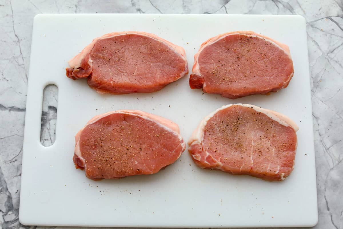 My Hawaiian pork chops are sweet, savory, colorful, and so easy! Pork chops simmer in a pineapple sauce with bell peppers, making the whole skillet irresistible. Serve it over rice so you can catch every drop of that delicious sauce. Pork chops seasoned and resting on a cutting board.