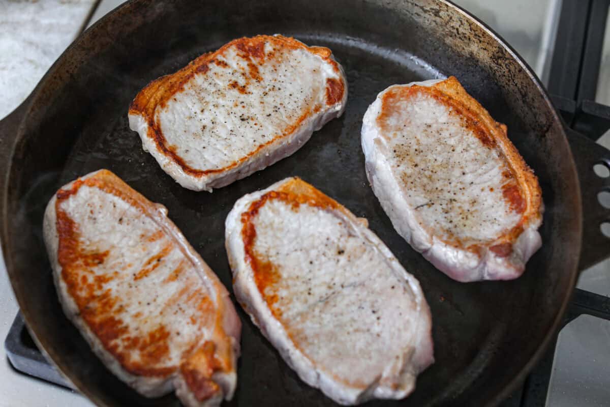 My Hawaiian pork chops are sweet, savory, colorful, and so easy! Pork chops simmer in a pineapple sauce with bell peppers, making the whole skillet irresistible. Serve it over rice so you can catch every drop of that delicious sauce. Seasoned pork chops being seared in a skillet.