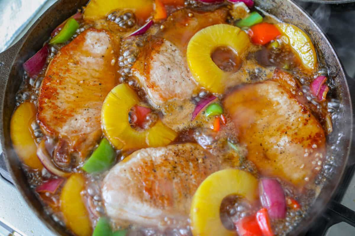 My Hawaiian pork chops are sweet, savory, colorful, and so easy! Pork chops simmer in a pineapple sauce with bell peppers, making the whole skillet irresistible. Serve it over rice so you can catch every drop of that delicious sauce. Pork chops, veggies and pineapples added to the sauce in the skillet to continue to cook.