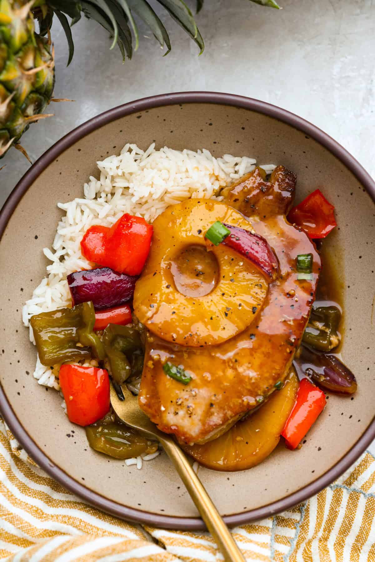 My Hawaiian pork chops are sweet, savory, colorful, and so easy! Pork chops simmer in a pineapple sauce with bell peppers, making the whole skillet irresistible. Serve it over rice so you can catch every drop of that delicious sauce. Plated Hawaiian pork chops on a bed of rice.