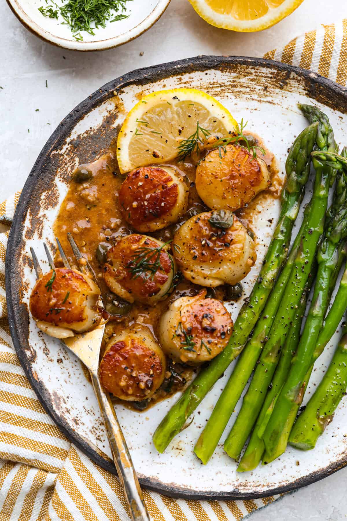 My pan seared scallops recipe has been a reader favorite for years, and one bite will show you why. The buttery golden scallops with that bright, fresh lemon flavor are what make this recipe stand out from all the others. Plated pan seared scallops with asparagus.