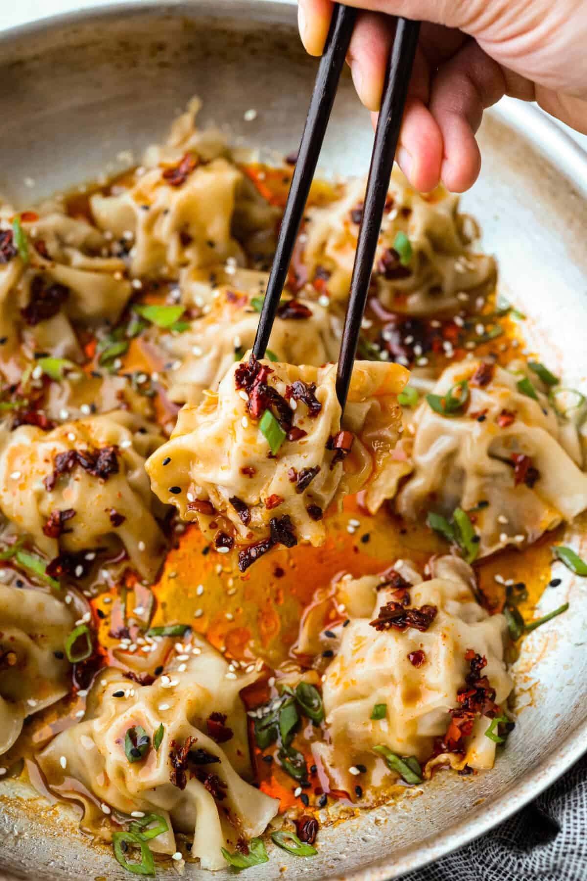 Someone lifting a blanket dumpling out of the pan with chopsticks. 