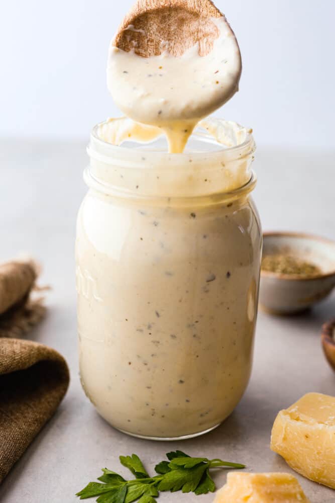 Jar of Alfredo sauce with a wooden spoon pouring sauce into it. 