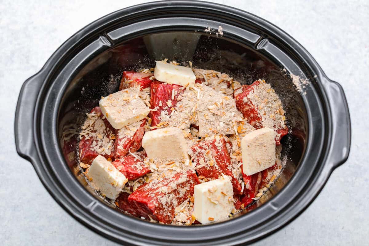 Cooks the chuck roast low and slow until it is tender, j Onion soup mix and butter added to the beef in the slow cooker.