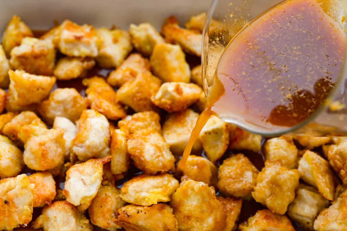 Someone pouring the sauce over pan fried chicken pieces before it gets baked.