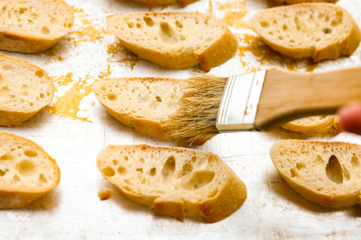 Sliced baguettes being spread with olive oil to broil. 