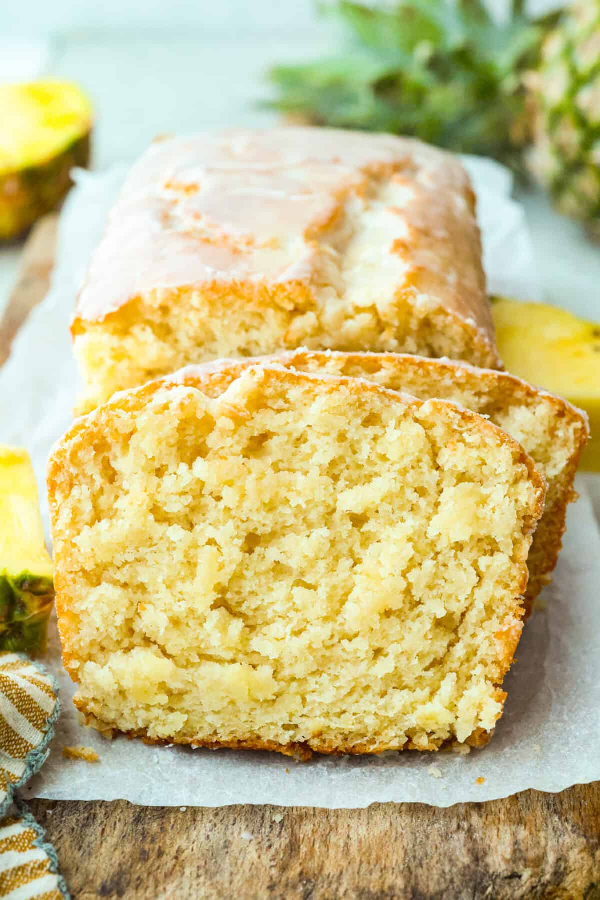 This glazed pineapple bread is what happens when a cozy quick bread meets a tropical vacation. Moist, tender, and drizzled with a sweet pineapple glaze, it's a taste of paradise in every bite. Sliced glazed pineapple bread on a cutting board.