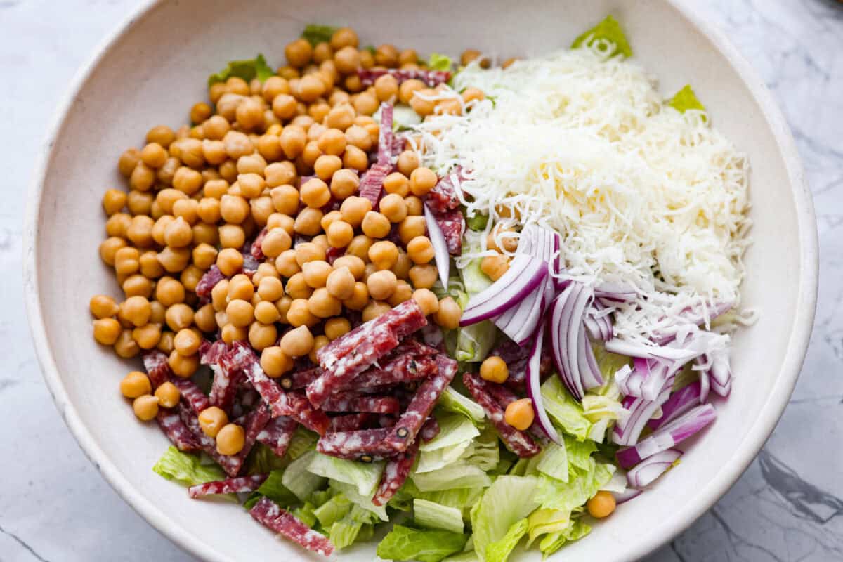This copycat La Scala Salad is the famous Italian chopped salad from Beverly Hills that Kim Kardashian is rumored to love. It’s fresh, crunchy, and packed with chickpeas, salami, mozzarella, and zesty red wine vinaigrette. Salad ingredients added to a large bowl.