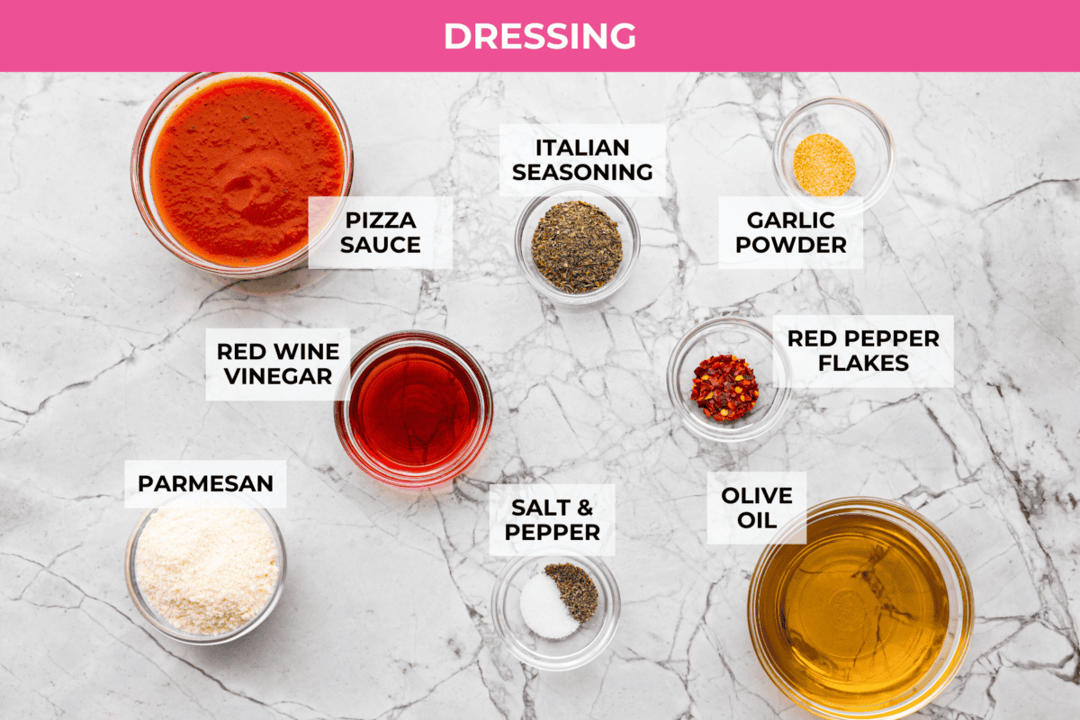 Pizza pasta salad is a fun twist on two family favorites! It's packed with pepperoni, mozzarella, fresh veggies, and a tangy pizza-inspired dressing. Get out of your pasta salad rut and make this unique and incredibly flavorful recipe! Overhead shot of labeled dressing ingredients.