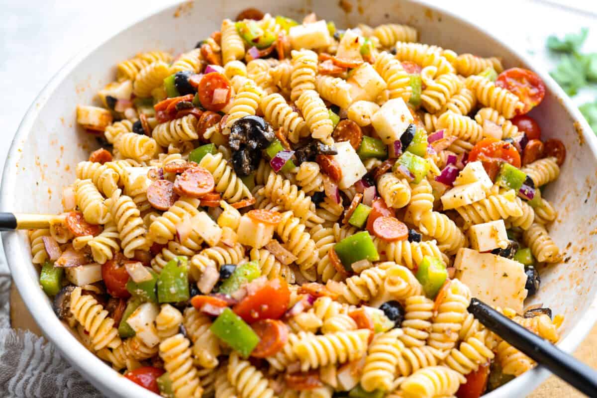 Pizza pasta salad is a fun twist on two family favorites! It's packed with pepperoni, mozzarella, fresh veggies, and a tangy pizza-inspired dressing. Get out of your pasta salad rut and make this unique and incredibly flavorful recipe! Pasta, veggies, meats and cheese all mixed together with the dressing.