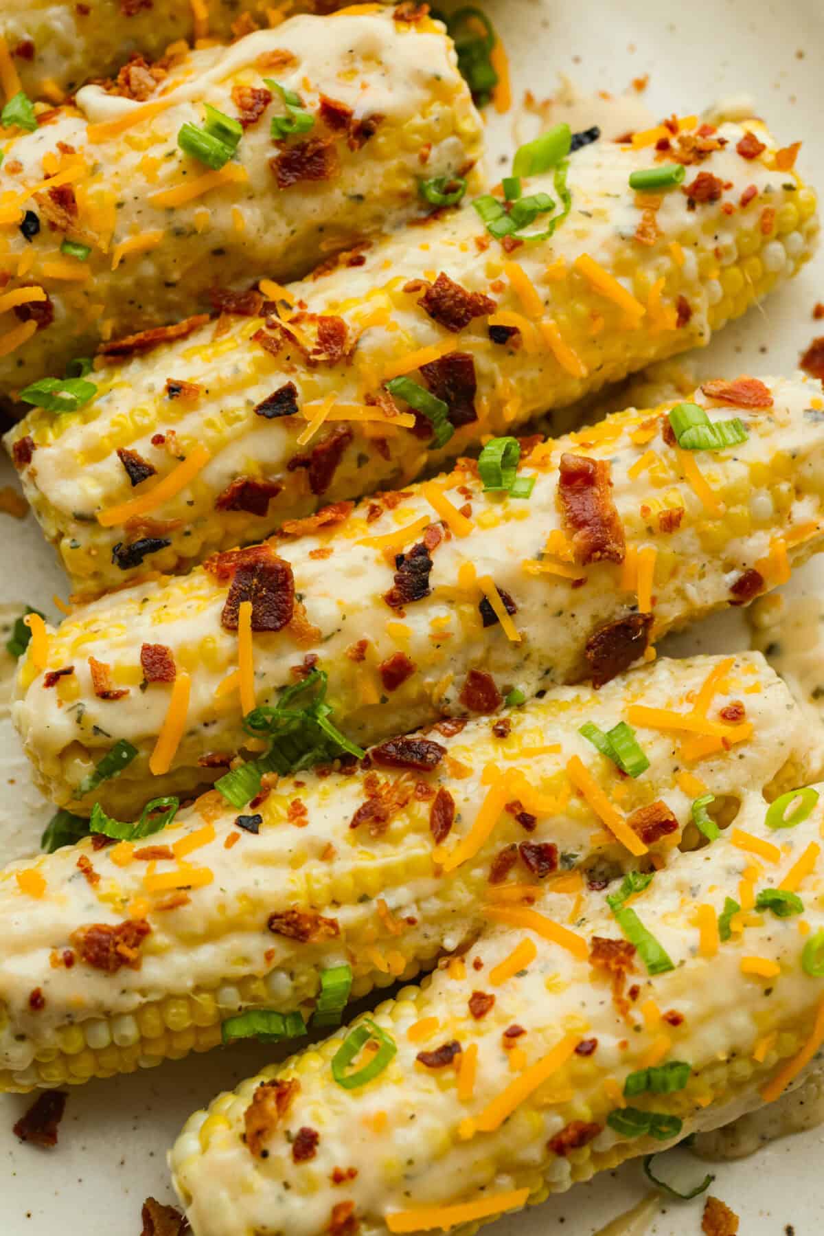 My crack corn on the cob takes summer corn to a whole new level! Smothered in a creamy ranch sauce and topped with bacon, cheddar, and green onions, it's the kind of side dish that disappears before the main course even hits the table. Crack corn on the cob on a serving platter, covered in green onions and bacon.