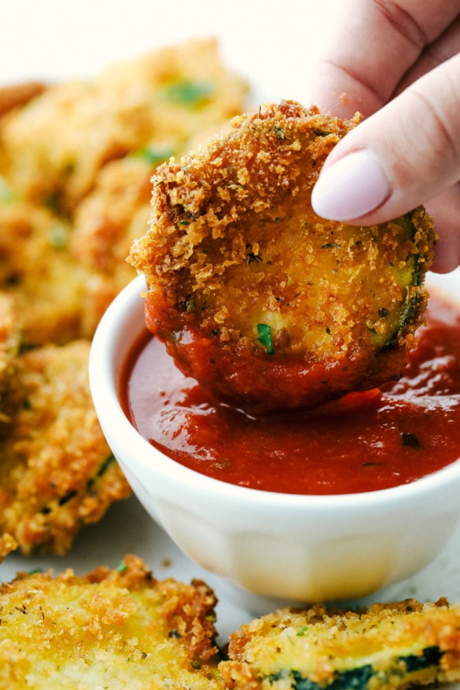 When my garden is overflowing with zucchini, this crispy Parmesan fried zucchini is one of my favorite things to make. It’s ready in just 15 minutes and is perfect as a quick appetizer, snack, or easy side with ranch, marinara, or fry sauce. Dipping a fried zucchini slice in marinara sauce.