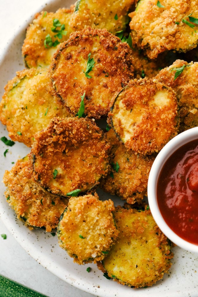 When my garden is overflowing with zucchini, this crispy Parmesan fried zucchini is one of my favorite things to make. It’s ready in just 15 minutes and is perfect as a quick appetizer, snack, or easy side with ranch, marinara, or fry sauce. Crispy Parmesan Fried Zucchini on a white plate with marinara sauce.