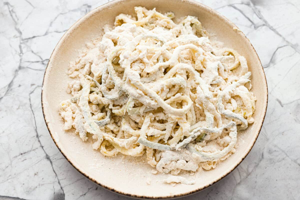 These crispy zucchini strings are golden, crunchy, and seriously hard to stop eating. Lightly battered and fried until perfectly crisp, they turn simple zucchini into an addictive snack or side dish that everyone will reach for first. Coating in the flour mixture.