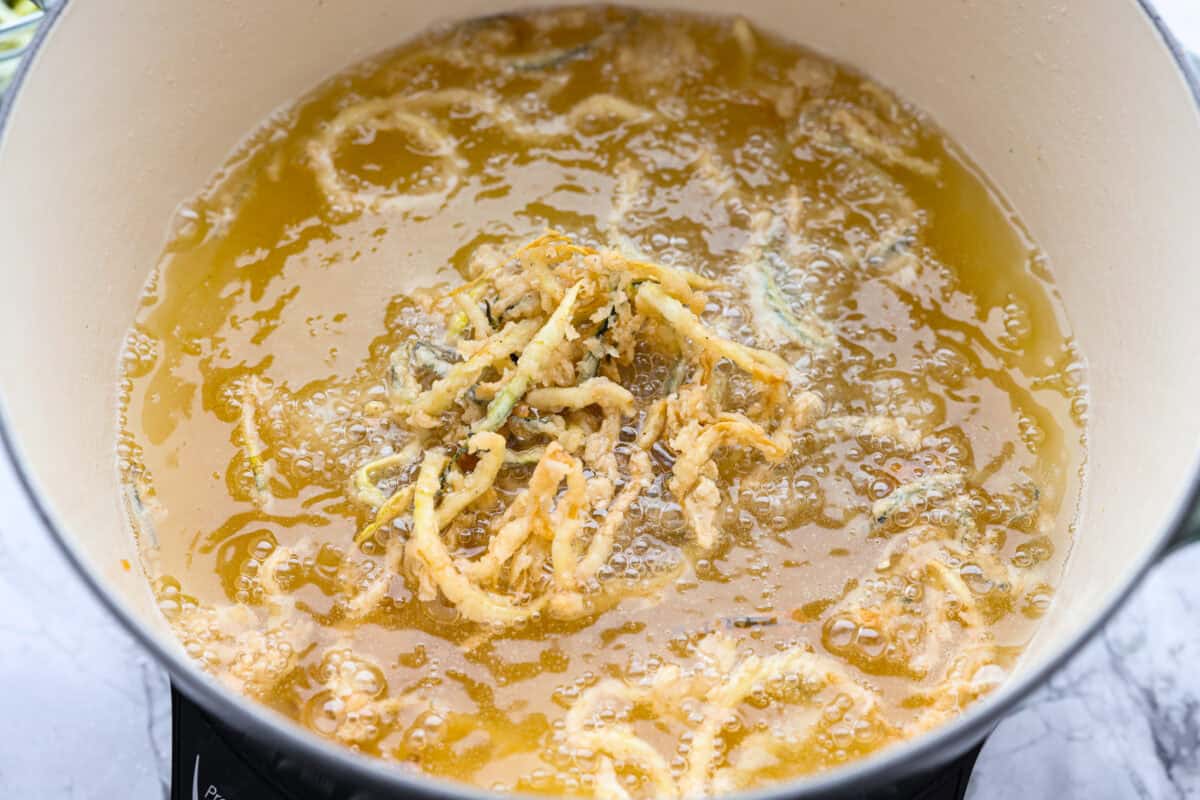 These crispy zucchini strings are golden, crunchy, and seriously hard to stop eating. Lightly battered and fried until perfectly crisp, they turn simple zucchini into an addictive snack or side dish that everyone will reach for first. Strings frying in oil.
