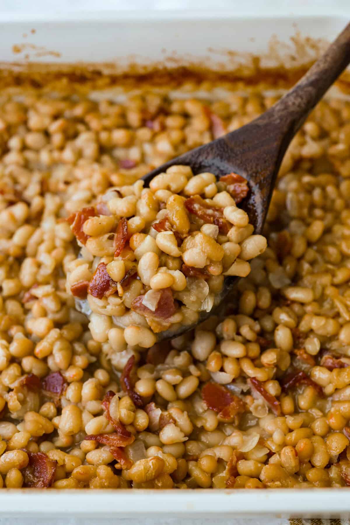 Someone lifting up a spoonful of the beans from the baking dish. 